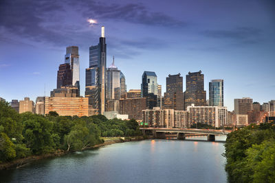 Modern buildings by river against sky in city