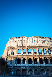 Low angle view of coliseum against clear blue sky