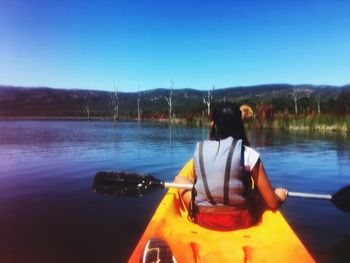 Man in boat on lake against clear blue sky