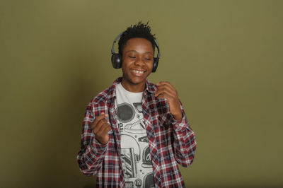 Young african american guy listens to music on headphones and dances on a green background