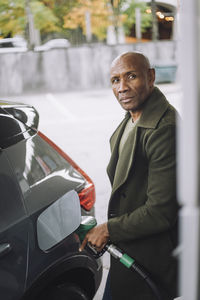 Mature man with shaved head refueling car at fuel station