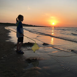 Full length of man standing at beach against sky during sunset