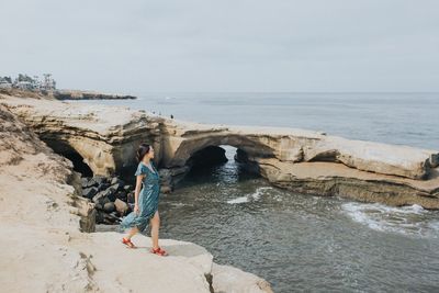 Man standing on rock by sea against sky