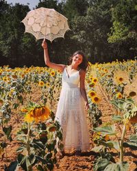 Portrait of woman holding umbrella while standing on sunflower land