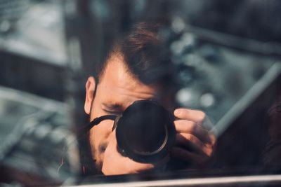 Reflection of man photographing with camera seen on glass