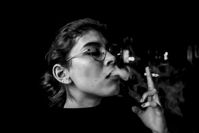 Close-up of woman smoking cigarette against black background