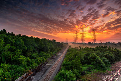 Railway tracks amidst trees against sky during sunset