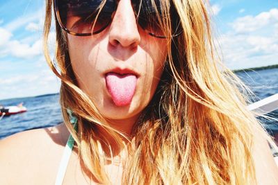 Close-up portrait of woman wearing sunglasses while sticking tongue out on sunny day