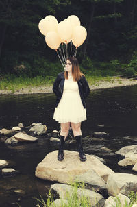 Woman blowing bubble gum while standing on rock at lake