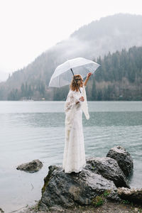 A beautiful young woman bride in a wedding lace dress stands in the middle of a lake and mountains