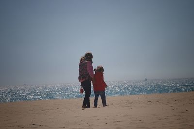 Rear view of mother and daughter on beach against clear sky