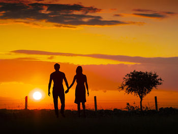 Silhouette couple walking on field against orange sky