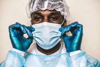 Portrait of doctor wearing mask sitting against colored background