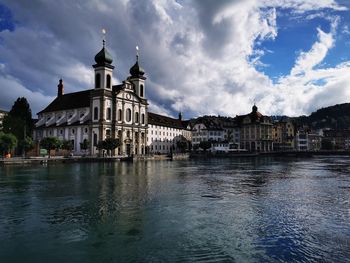 Buildings at waterfront against cloudy sky