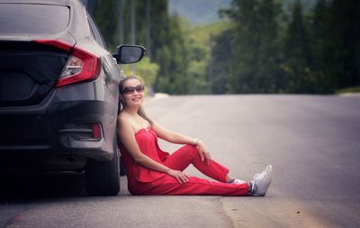 Portrait of woman in sunglasses sitting against car