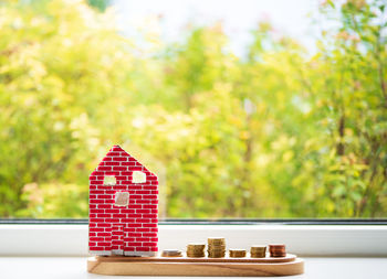 Model of house with coins on wooden table on blurred background