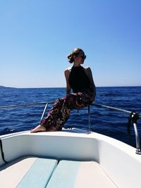 Man sitting on boat in sea against clear blue sky