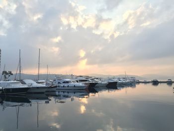 Boats moored at harbor against cloudy sky during sunset