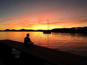 Silhouette man sitting on jetty against sea during sunset