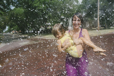 Playful mother carrying daughter while enjoying in fountain at park