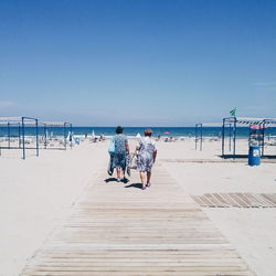 Rear view of women walking on boardwalk at beach against sky