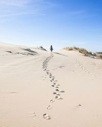 Rear view of woman walking on sand at desert against sky during sunny day