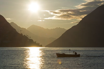 Silhouetted view of boat on river by mountains at disk