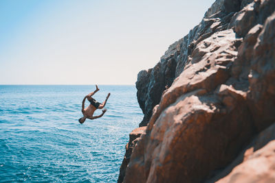 Man standing on rock by sea against clear sky