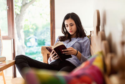 Teenage girl reading book while sitting on sofa