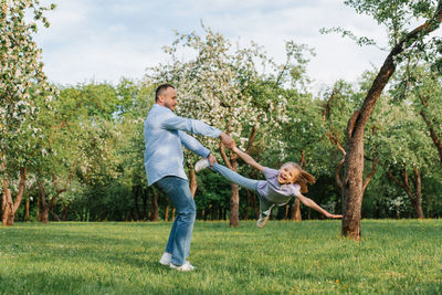 Cheerful father twists his smiling daughter by the hand and by the leg around him during a walk