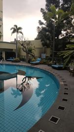 Swimming pool by palm tree against sky