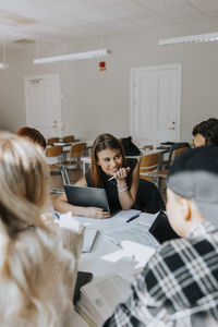 Smiling teenage girl sitting with friends while studying in classroom