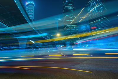 Light trails on road by illuminated buildings in city at night