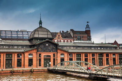 Arch bridge over river by buildings against sky in city