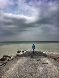 Rear view of woman standing on jetty against cloudy sky