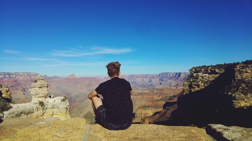 Rear view of hiker looking at rocky mountain against blue sky