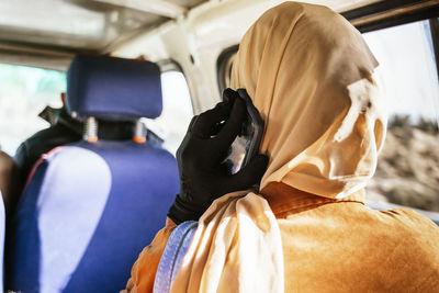 Back view of anonymous female traveler in stylish headscarf having phone conversation while sitting in car during trip in egypt