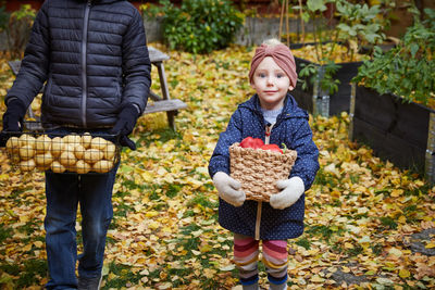 Portrait of smiling girl with vegetable basket while standing by male sibling in back yard