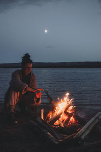 Woman sitting by campfire on beach