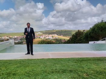 Businessman standing by infinity pool against cloudy sky