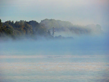 View of calm sea against mountain in foggy weather