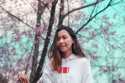 Portrait of beautiful young woman standing against trees