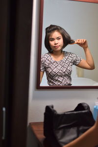 Young woman combing hair reflecting on mirror at home