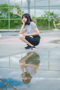 Reflection of thoughtful young woman on puddle at basketball court