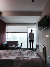 Rear view of man standing by window in hospital ward