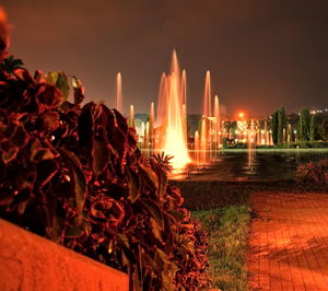 Illuminated fountain in city against sky at night