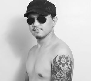 Portrait of young shirtless man wearing sunglasses and cap against wall