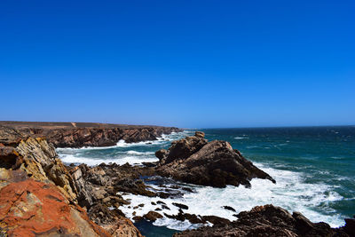 Rock formations in sea against clear blue sky