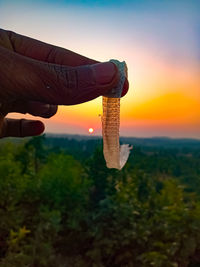 Person holding umbrella against sky during sunset
