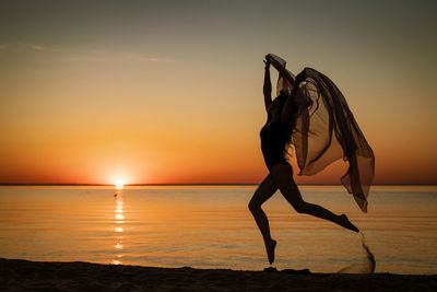 Young woman at sunset jumping on the seashore with background of the sky